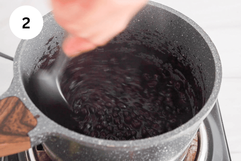 A spoon stirring blueberries in a small pot.