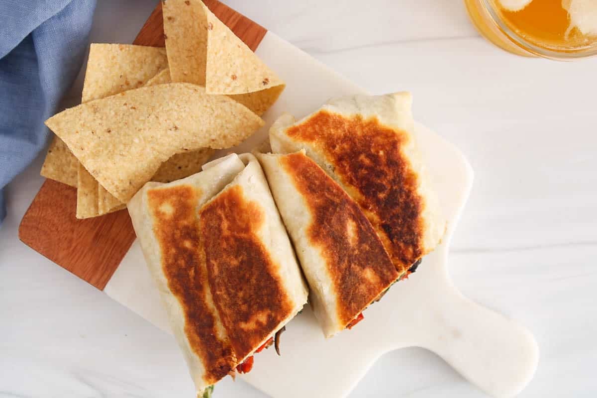 Roasted halves sandwich wraps on a white board with a side of chips.