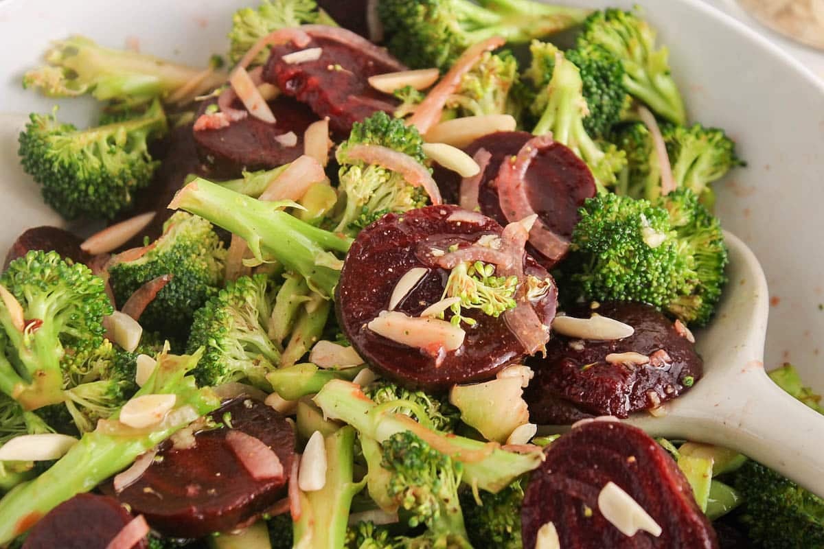 A broccoli beet salad in a large salad bowl with onions and almonds.