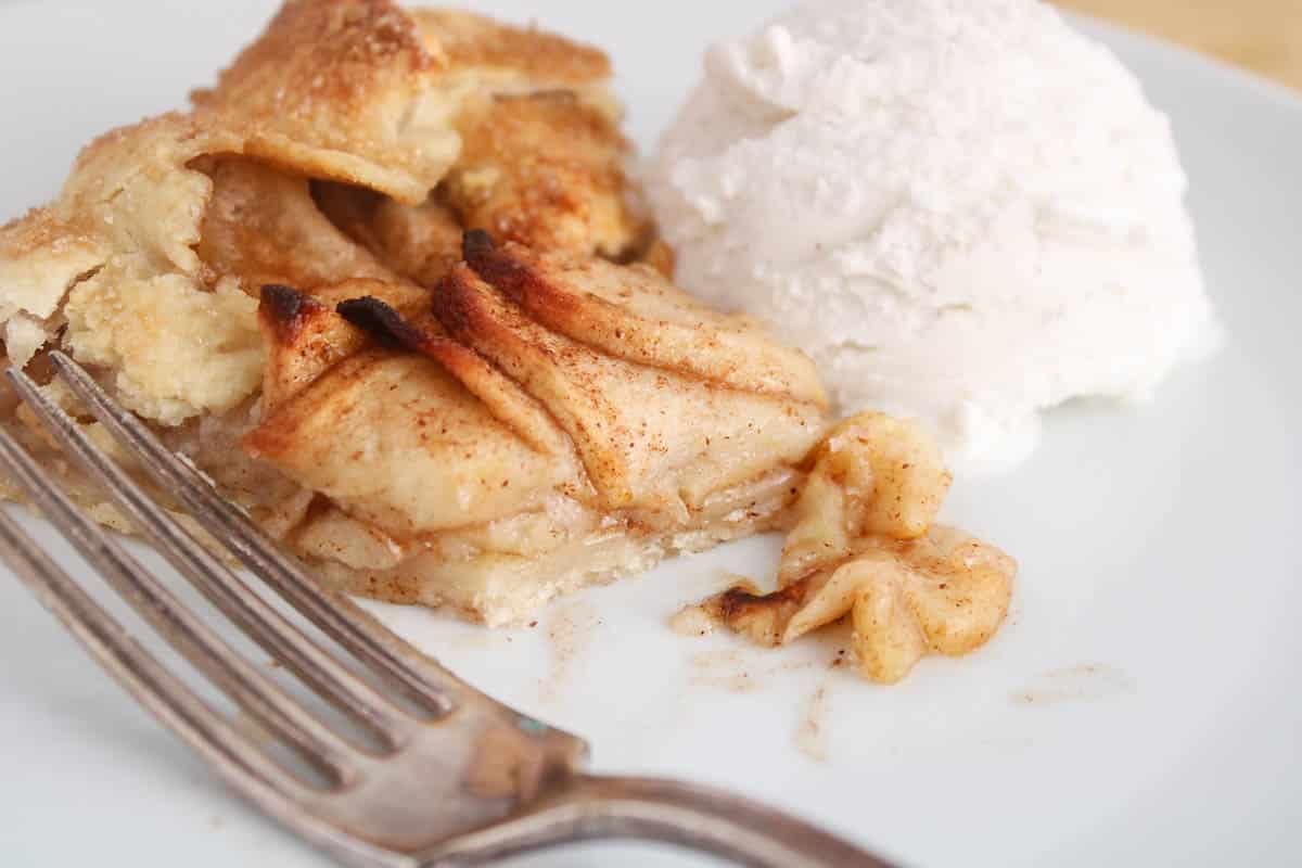 Slice of vegan apple galette with a scoop of vanilla ice cream on a plate with a bite taken off.