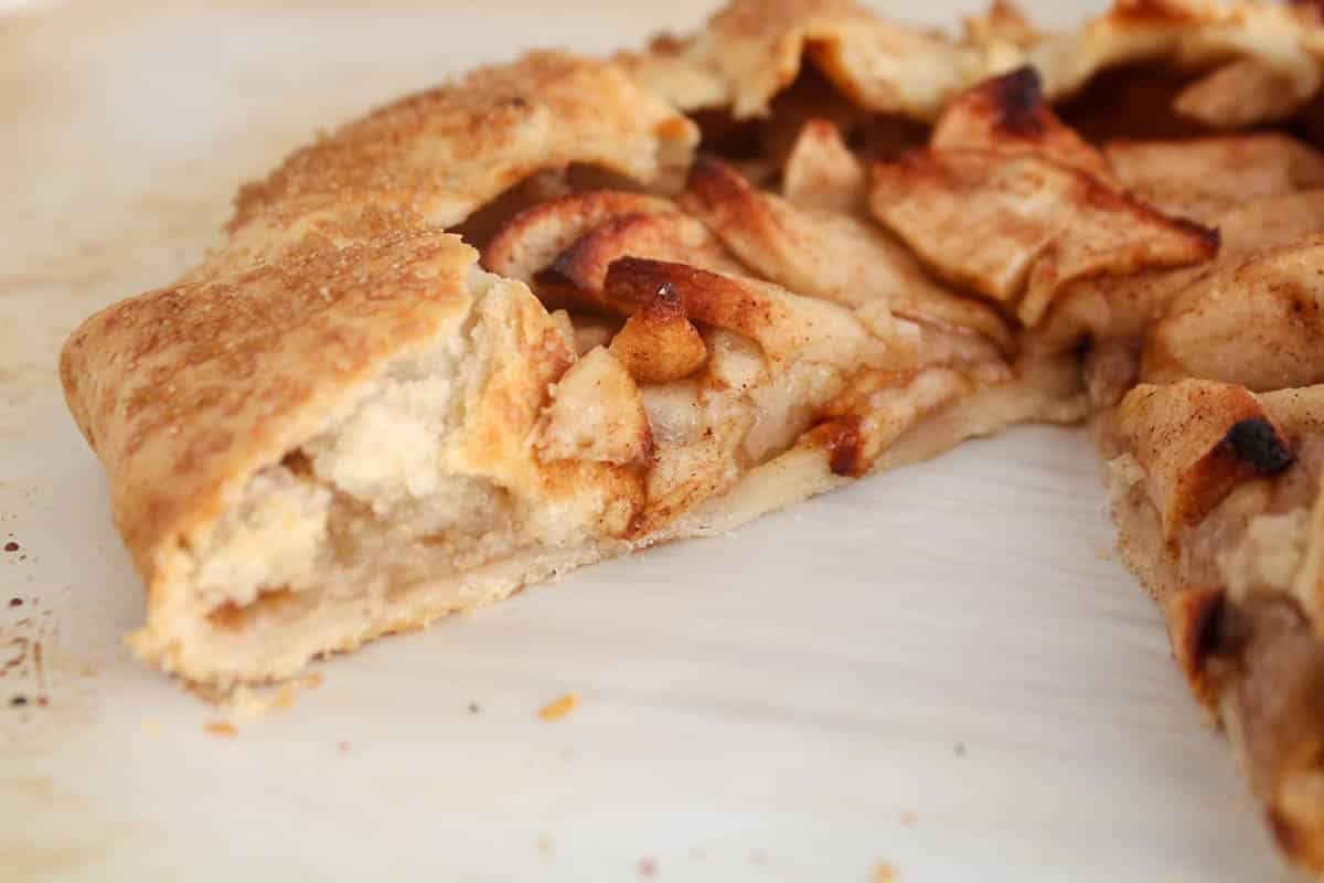 Vegan apple galette on parchment paper with a slice taken off showing the middle part.