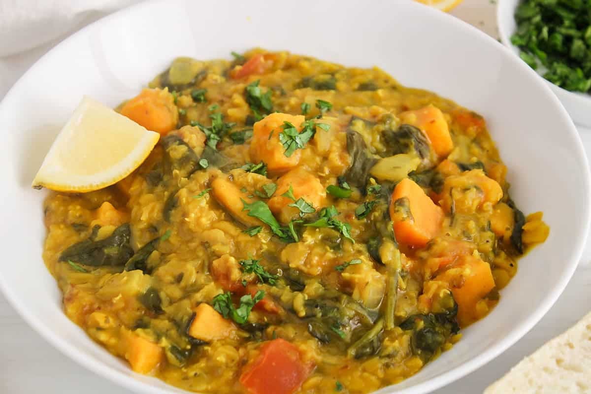 A white bowl filled with a sweet potato red lentil dhal with spinach and coconut milk.