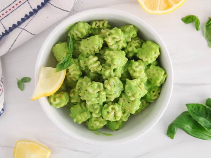 Green pea pasta sauce with short noodles and a side of lemon wedge and more fresh basil.