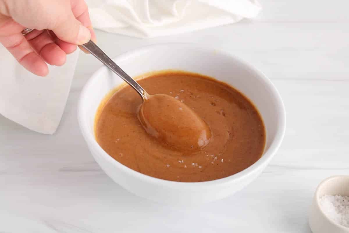A spoon taking some vegan peanut butter caramel from a white bowl.