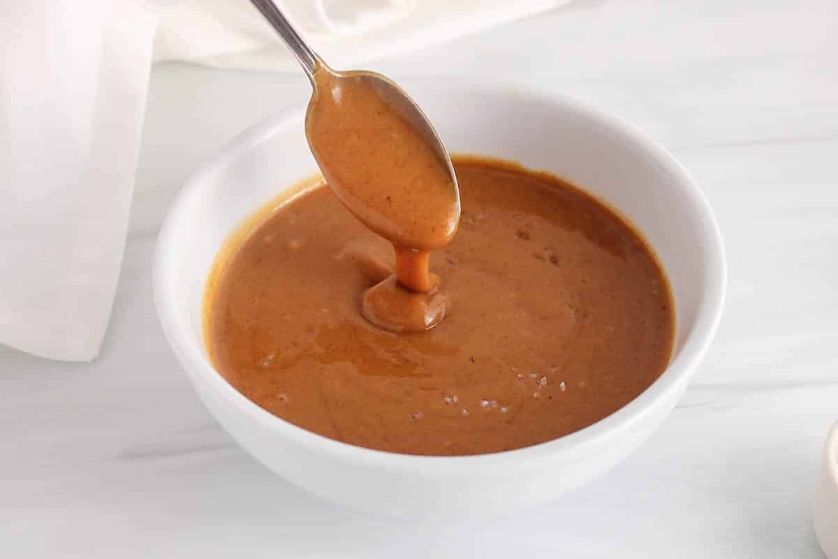 A spoon drizzling some salted peanut butter caramel back in a bowl to show texture.