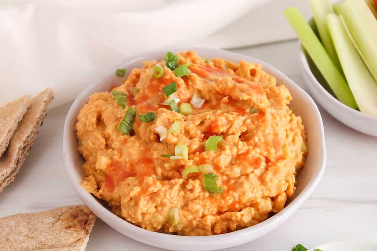 Vegan buffalo chickpea dip garnished with green onion and cayenne pepper hot sauce.