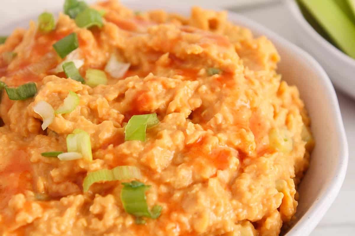 Creamy buffalo chickpea dip garnished with hot sauce and green onions.