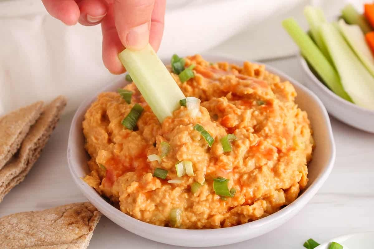 A stick of celery dipping in a buffalo chickpea dip.