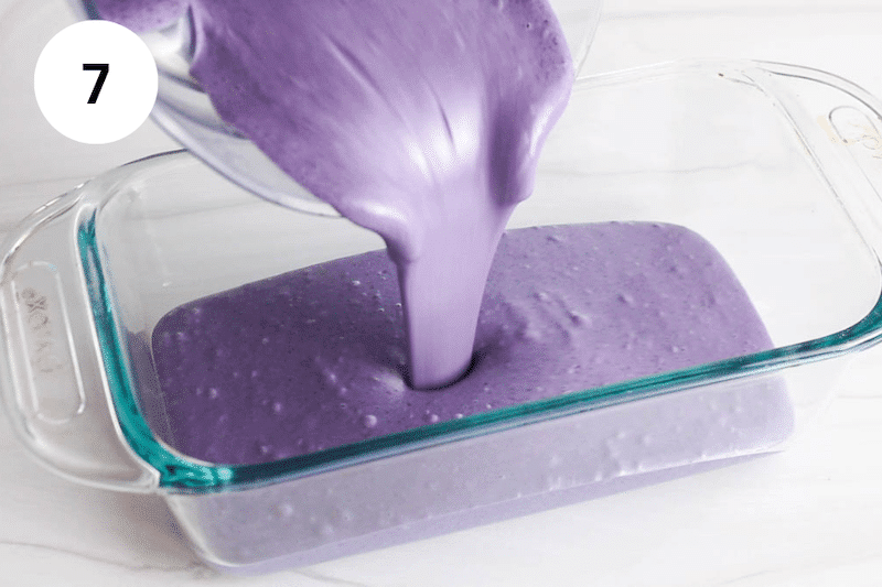 Pouring a blueberry creamy mixture in a glass container.
