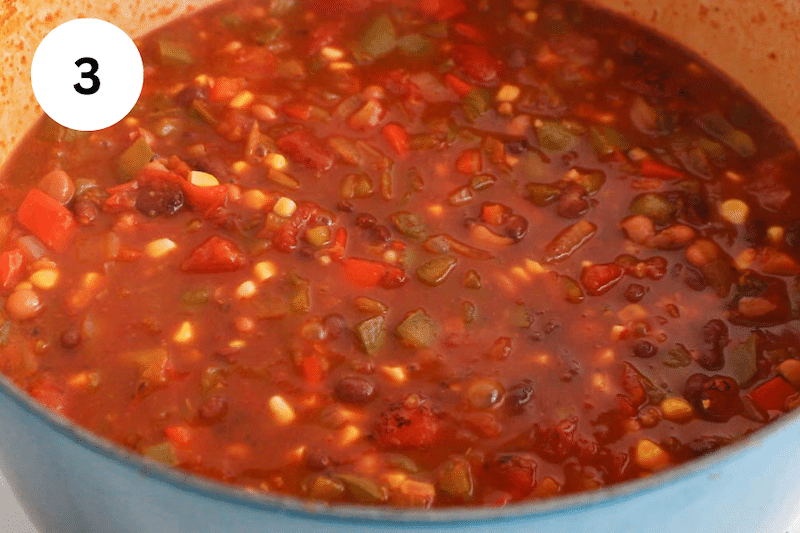 A bright red enchilada soup simmering in a large pot.