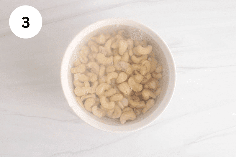 Cashews soaking in warm water in a white bowl.