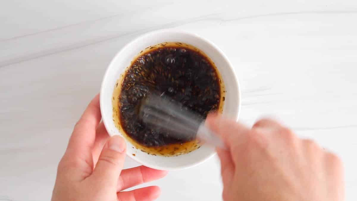 Small white bowl with a whisk stirring a dark sauce.