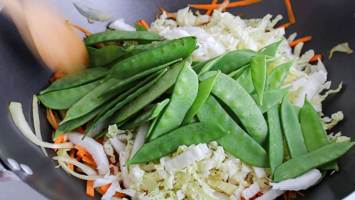 Large wok pan with some cabbage and snow peas cooking.