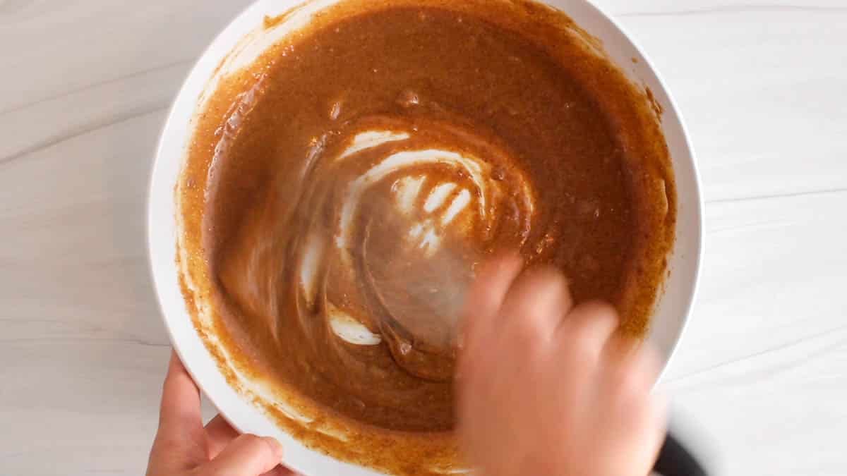 A large whisk stirring a brown batter mixture in a large white bowl.