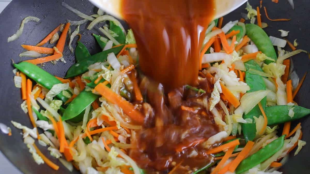 Large pan of cooking vegetables with a teriyaki sauce pouring.