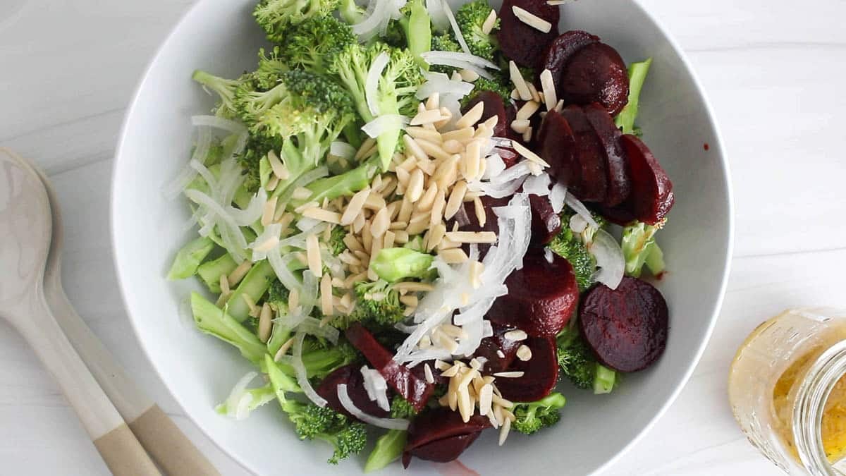 Large white bowl filled with broccoli, beets, onion and almonds.