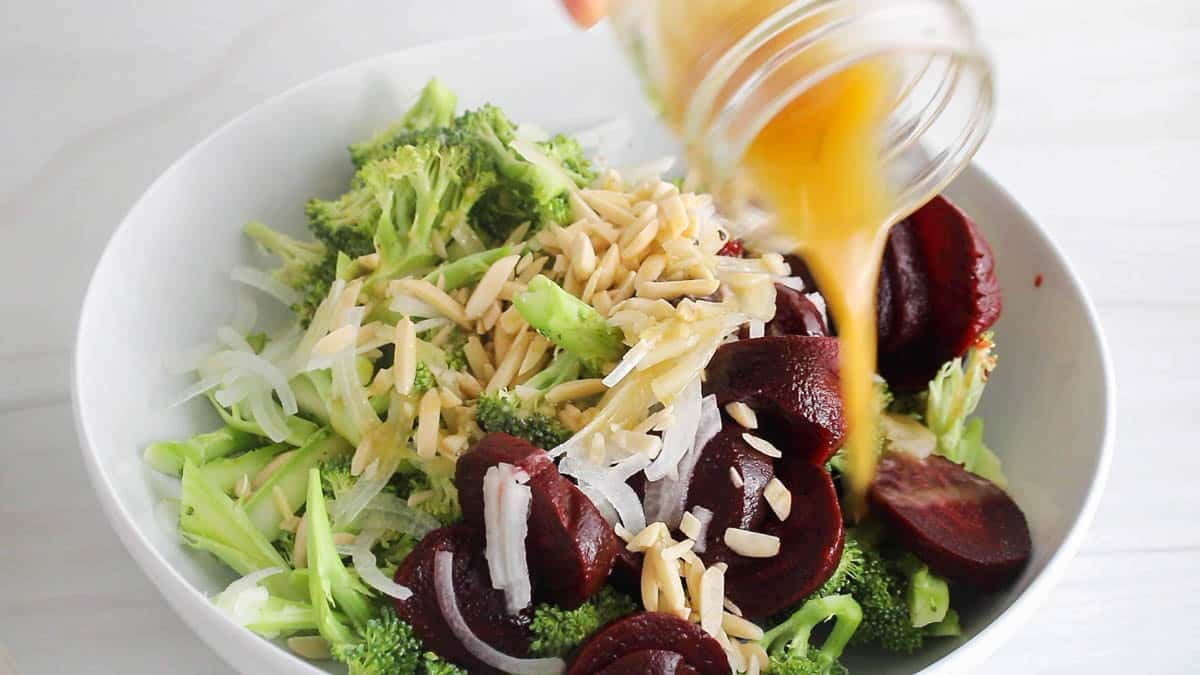 A dressing pouring over a bowl with vegetables.