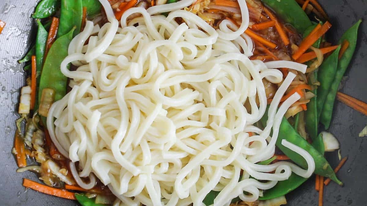 Large pan with teriyaki vegetables covered with udon noodles.