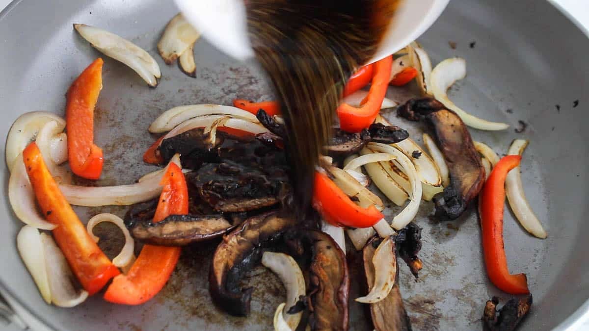 Dark sauce pouring over cooked vegetables in a large pan.
