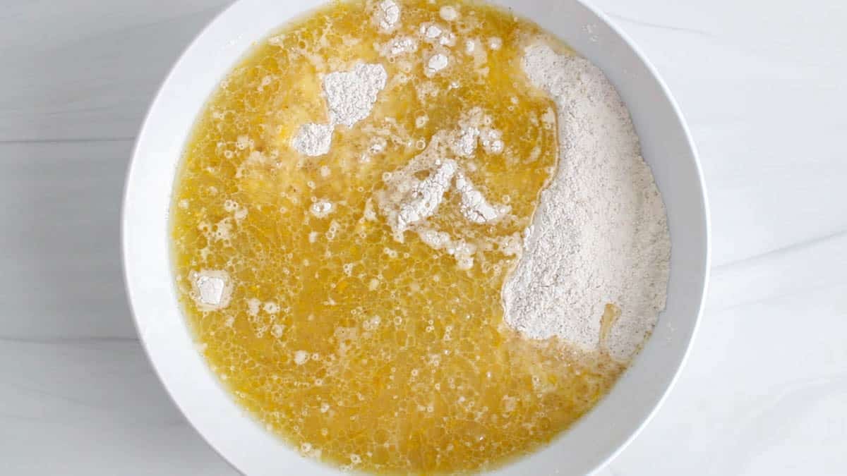 Large white bowl with a orange juice mixture over flour.