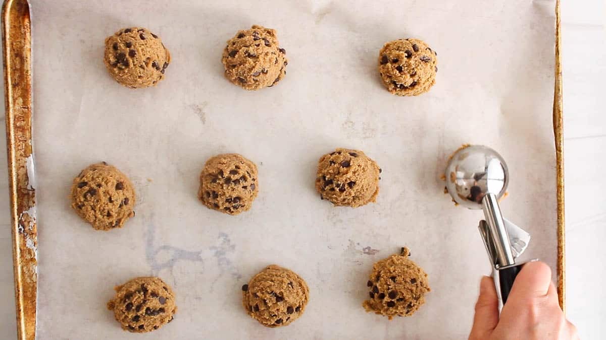 Ice cream scoop dividing the cookie batter over a baking sheet with parchment paper.