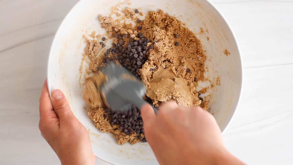 A spatula stirring a cookie dough mixture with chocolate chips.