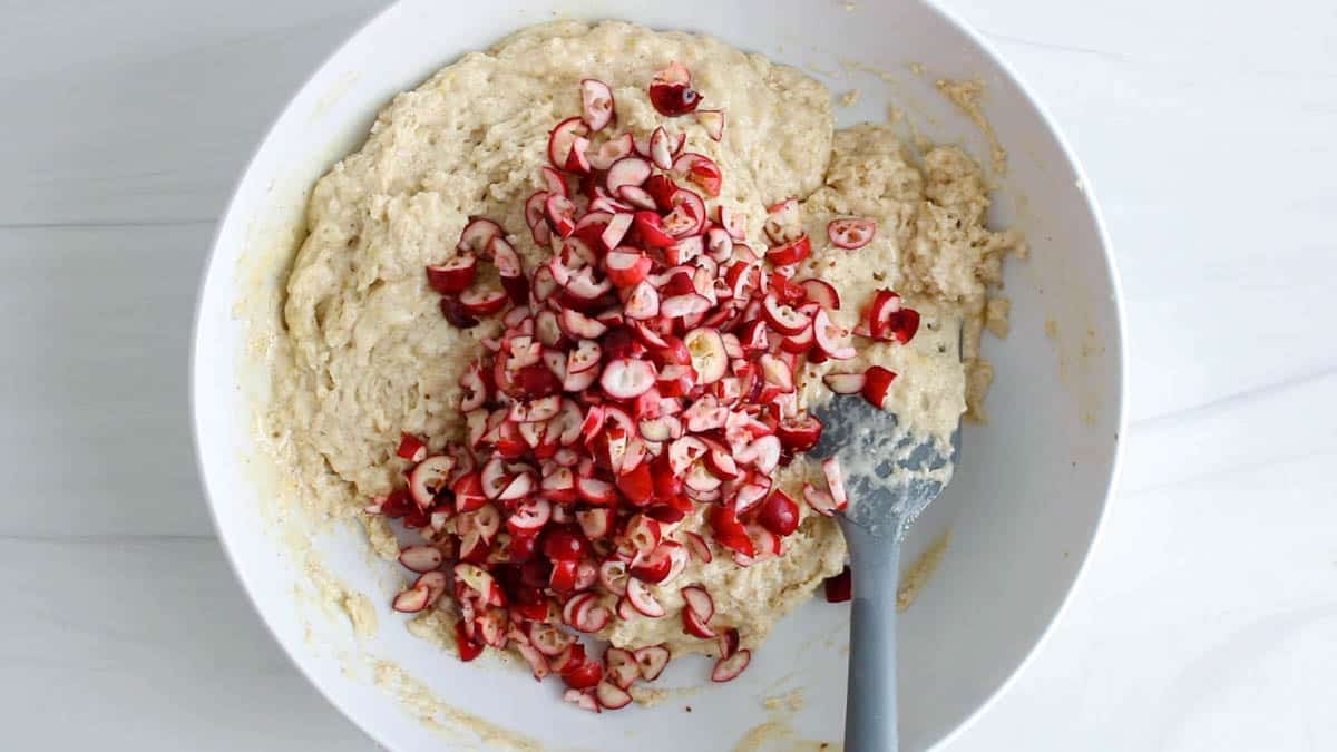 White bowl with a muffin batter topped by fresh cranberries.