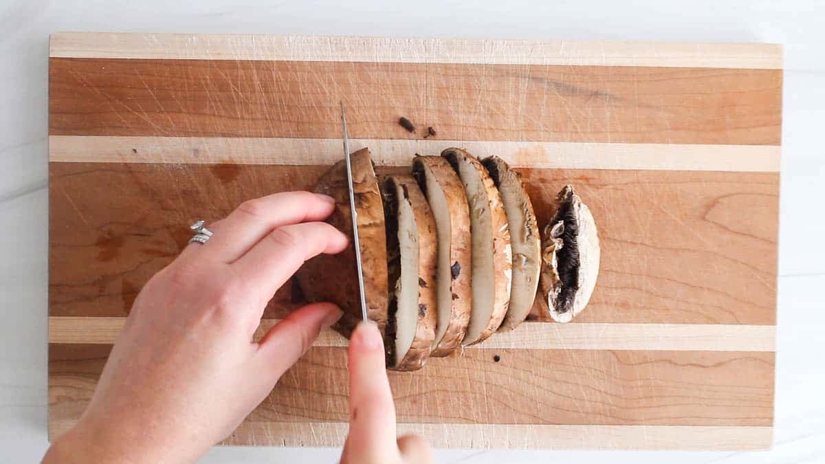A knife slicing a portobello mushroom into thick slices.