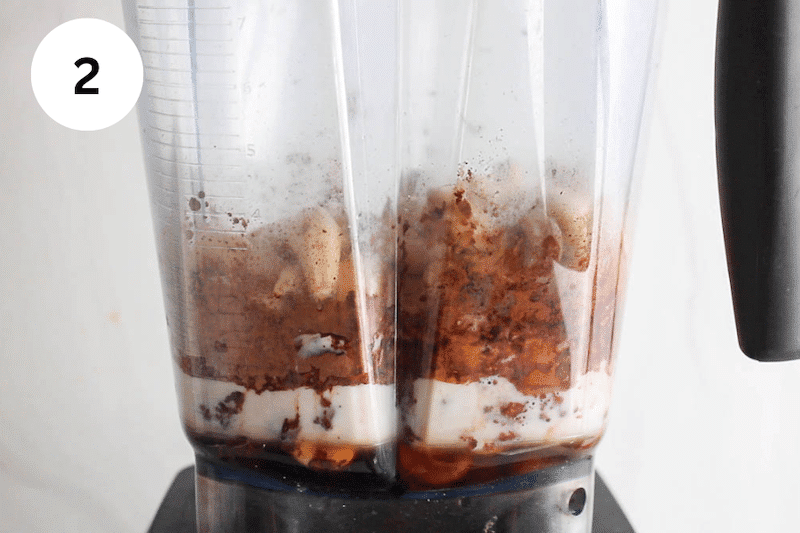 A blender with cashews, milk and cacao powder.