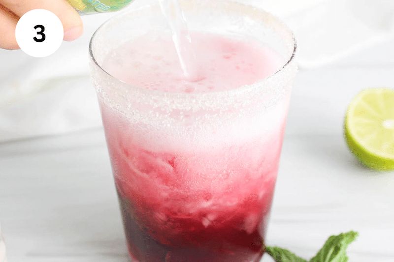 Pouring sparkling water in a glass of cranberry juice.
