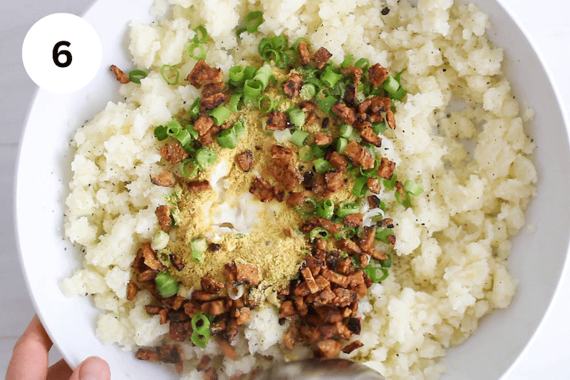 Mashed potatoes in a large bowl topped with vegan sour cream, vegan bacon and seasonings.
