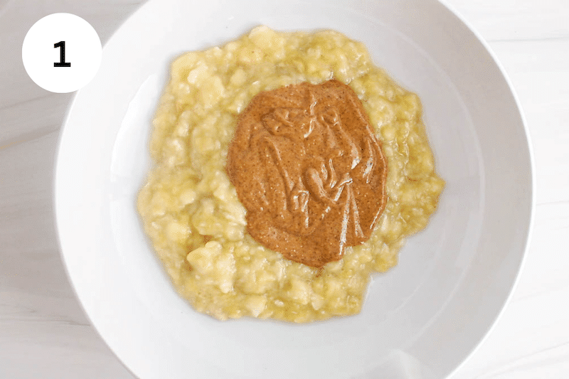 White bowl with mashed bananas and almond butter.