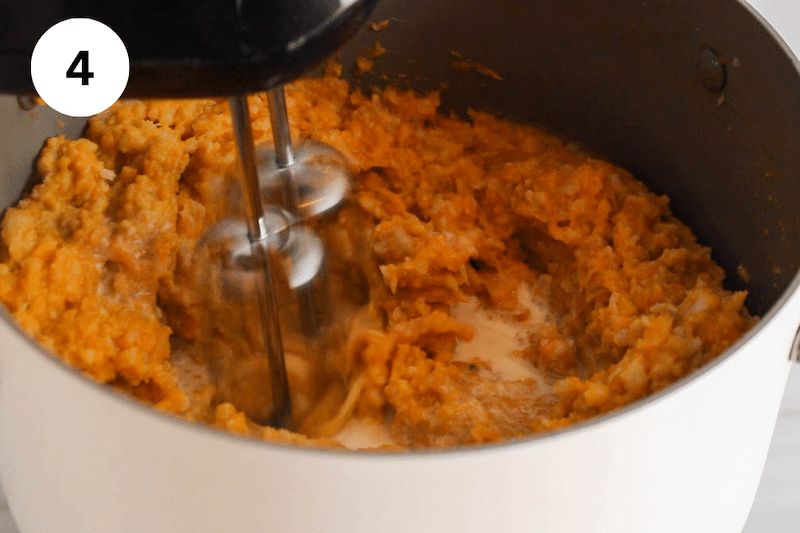 Electric beater mixing in a pot with mashed sweet potato and cauliflower.