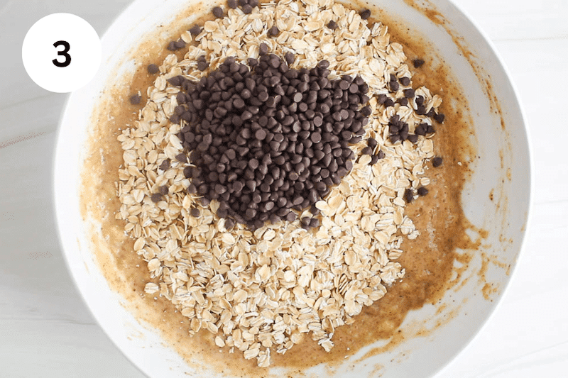 White bowl with a creamy mixture topped with rolled oats and chocolate chips.