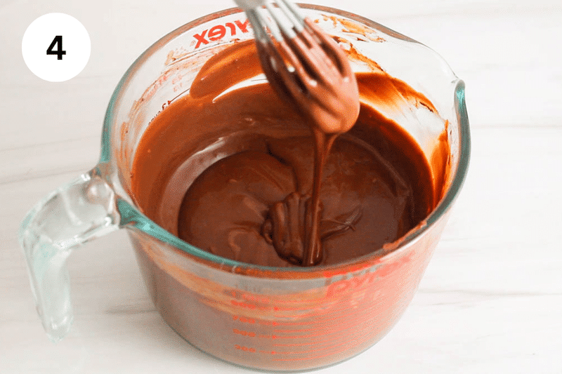 A small whisk drizzling a thick chocolate ganache in a glass container.