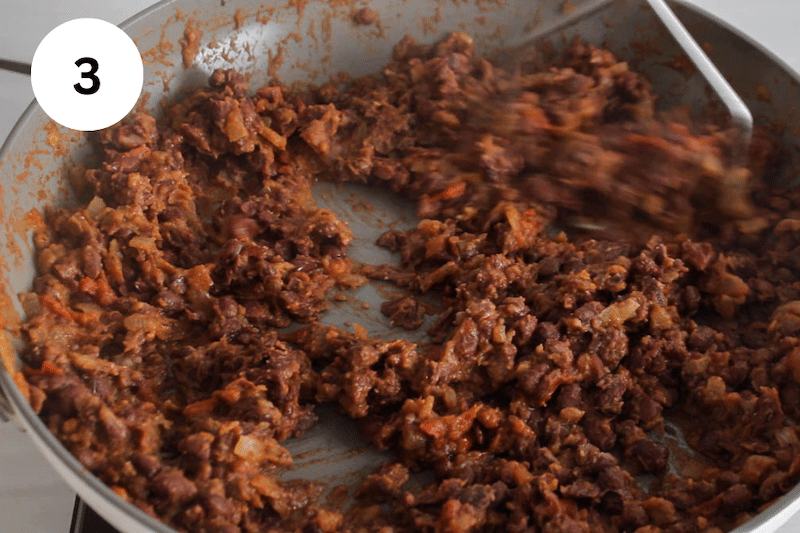 A potato masher mashing in a pan a black bean mixture.