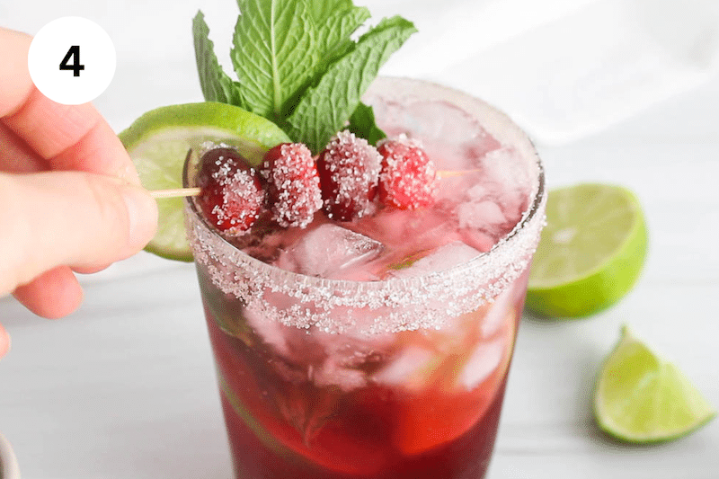 A hand decorating a glass of cranberry mocktail.