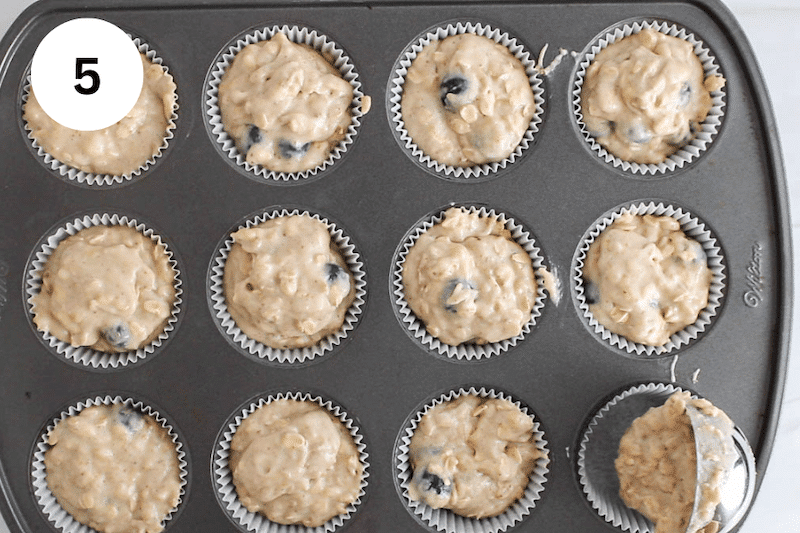 An ice cream scoop dividing a muffin batter in a muffin pan.