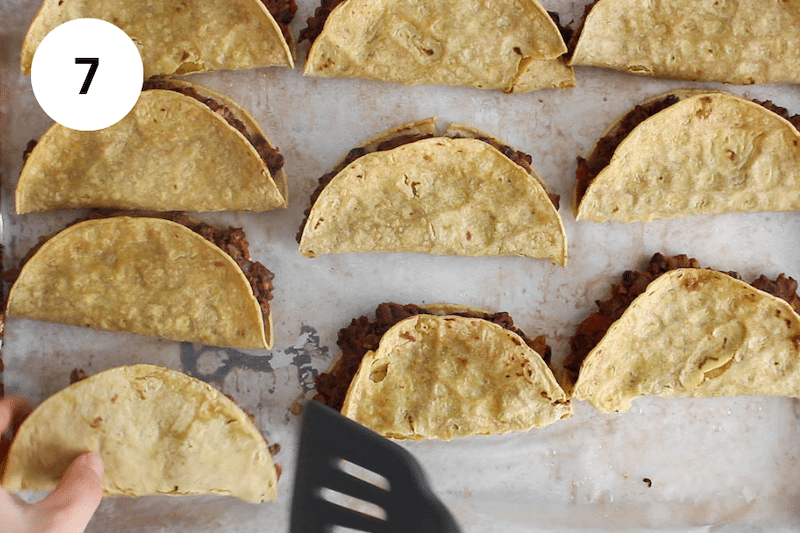A spatula flipping a baked taco on a baking sheet.
