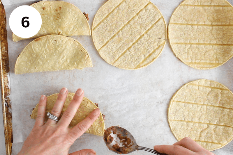 A hand folding a corn tortilla over black bean filling.