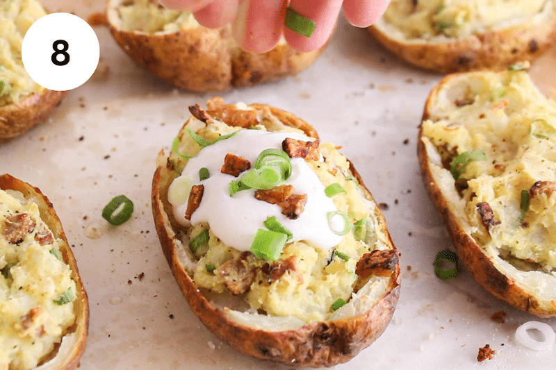 A hand garnishing baked potatoes with green onions.