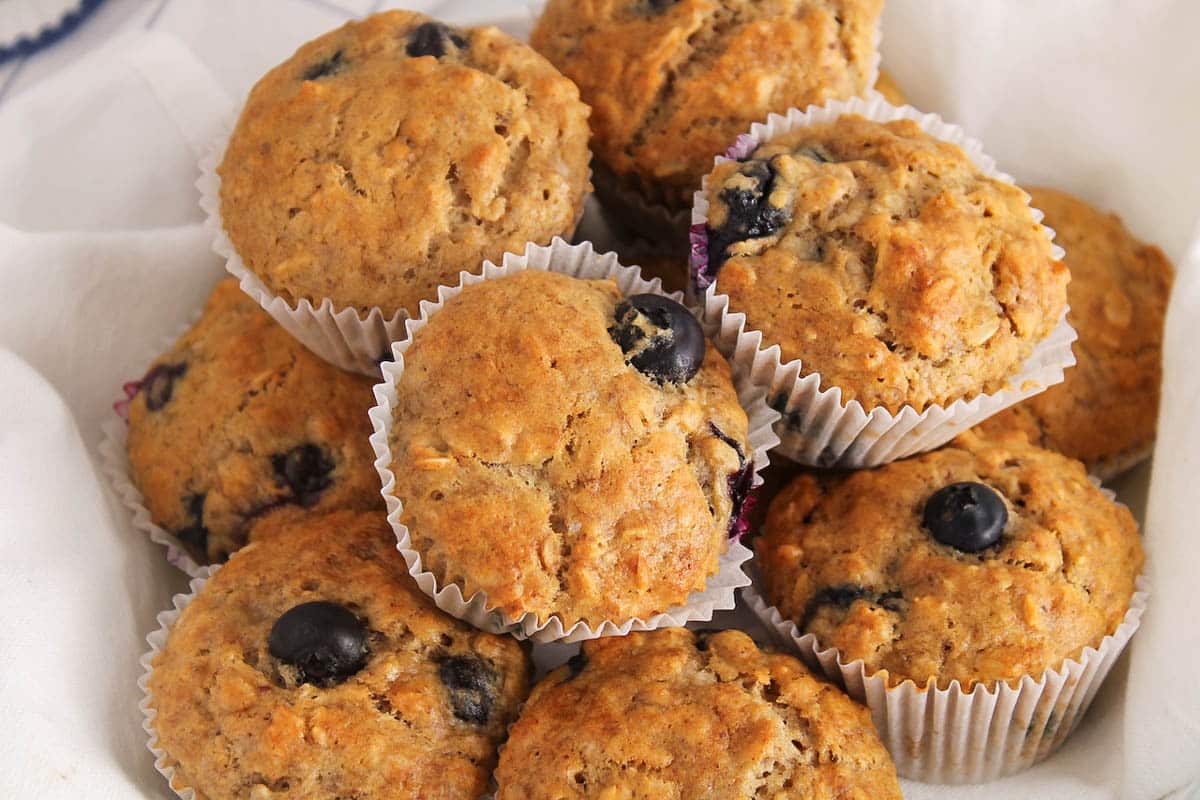 A pile of vegan banana blueberry oatmeal muffins over a white towel.
