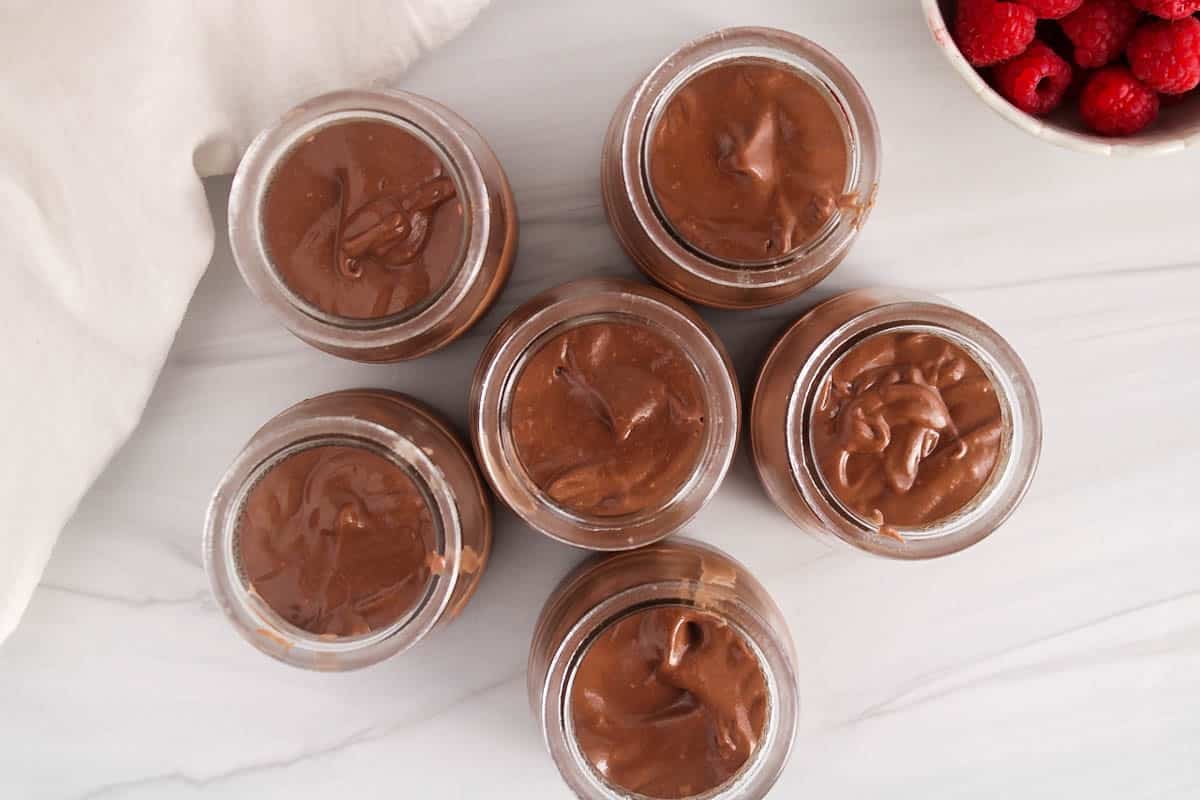 6 small jars of cashew chocolate mousse on a white table.
