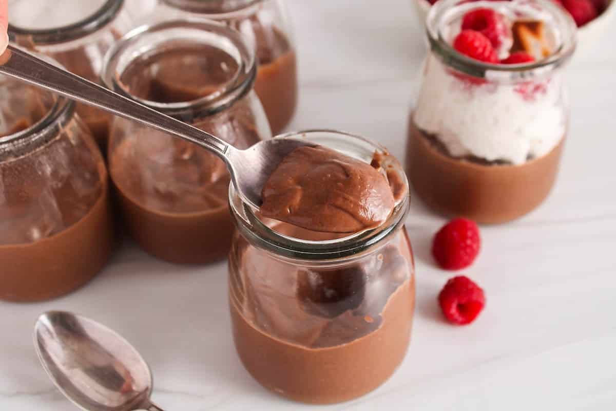 A spoon taking some chocolate cashew mousse for a small jar.