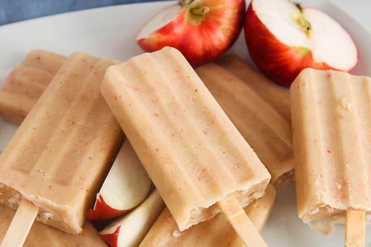 Apple popsicles on a white plate with sliced apple on the side.
