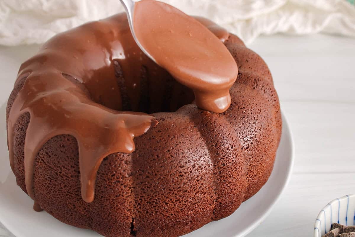 A large spoon pouring a vegan chocolate ganache over a chocolate bundt cake.