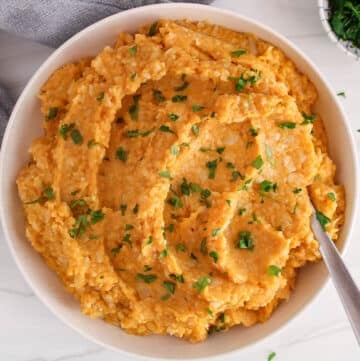A large white bowl with a mashed sweet potato and cauliflower mixture garnished with fresh parsley.