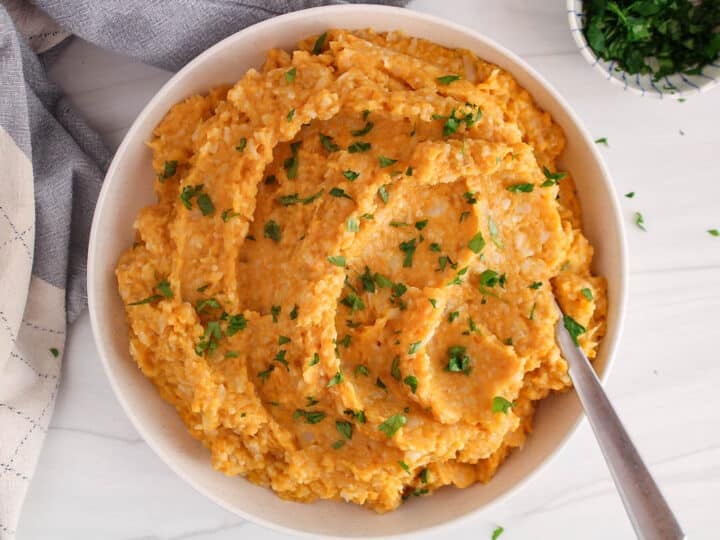 A large white bowl with a mashed sweet potato and cauliflower mixture garnished with fresh parsley.