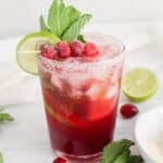 Non-alcoholic cranberry juice mocktail filled with ice cubes, lime wedges, fresh cranberries and mint.