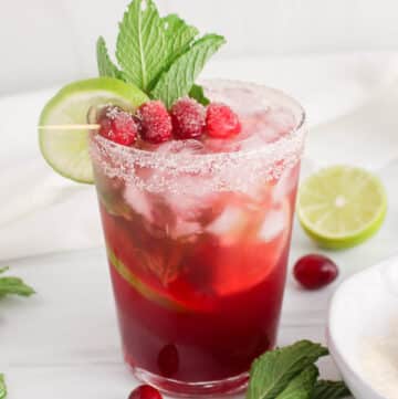 Non-alcoholic cranberry juice mocktail filled with ice cubes, lime wedges, fresh cranberries and mint.
